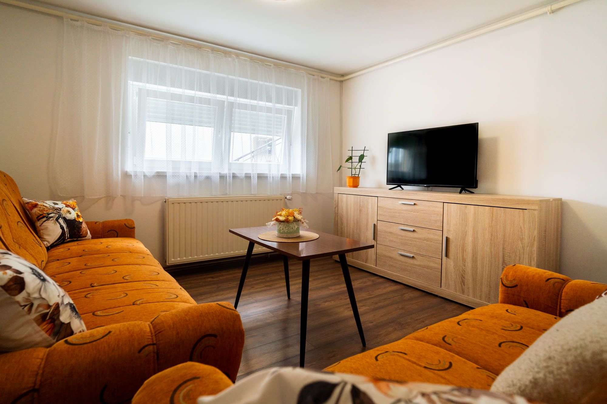 Wohnzimmer mit Fernseher, Sideboard und orangefarbenen Sofas